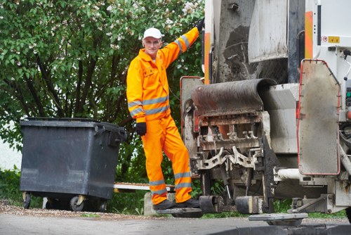 Worker clearing garden debris with wheelbarrow and tools