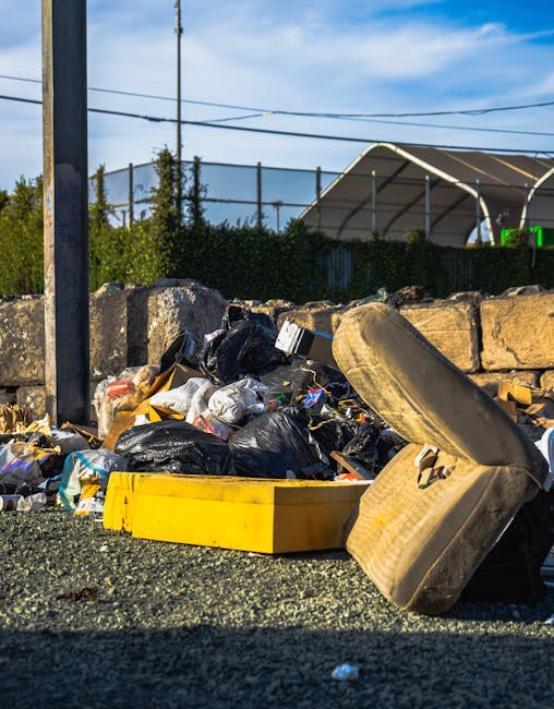 Three large black plastic garbage bags filled with waste sit on the pavement near the curb, leaning against a black metal fence. The bags appear to contain household rubbish, and they are slightly cru